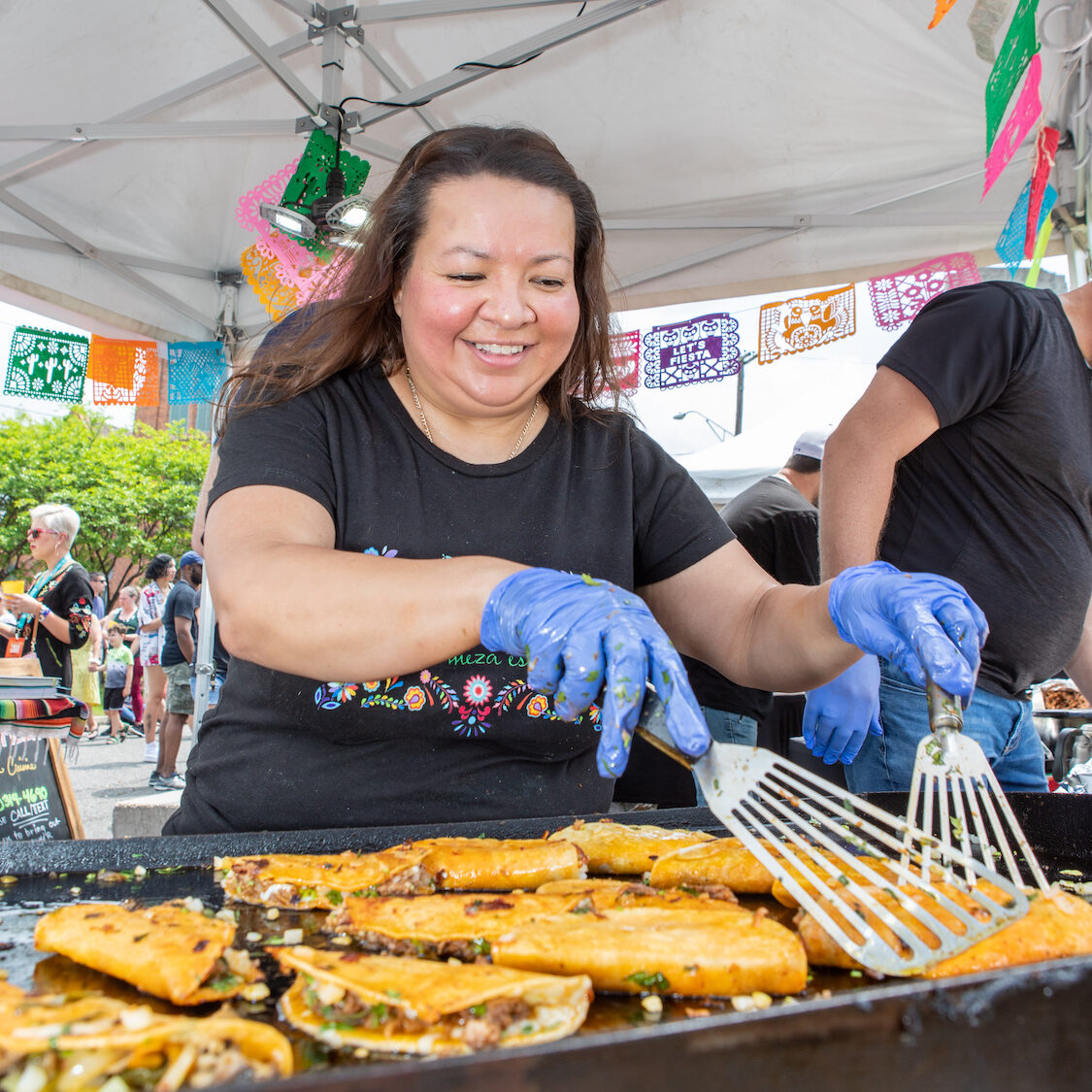 A taco vendor flips tacos with her spatulas.